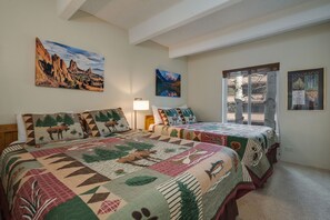 Une chambre avec deux lits, une grande fenêtre et des œuvres d’art murales représentant des paysages.