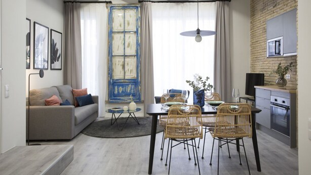Un espacio habitable compacto con comedor, kitchenette y un sofá con cojines.