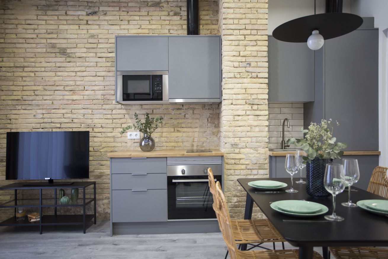 A modern kitchen with a brick wall, built-in microwave, oven, and grey cabinetry.