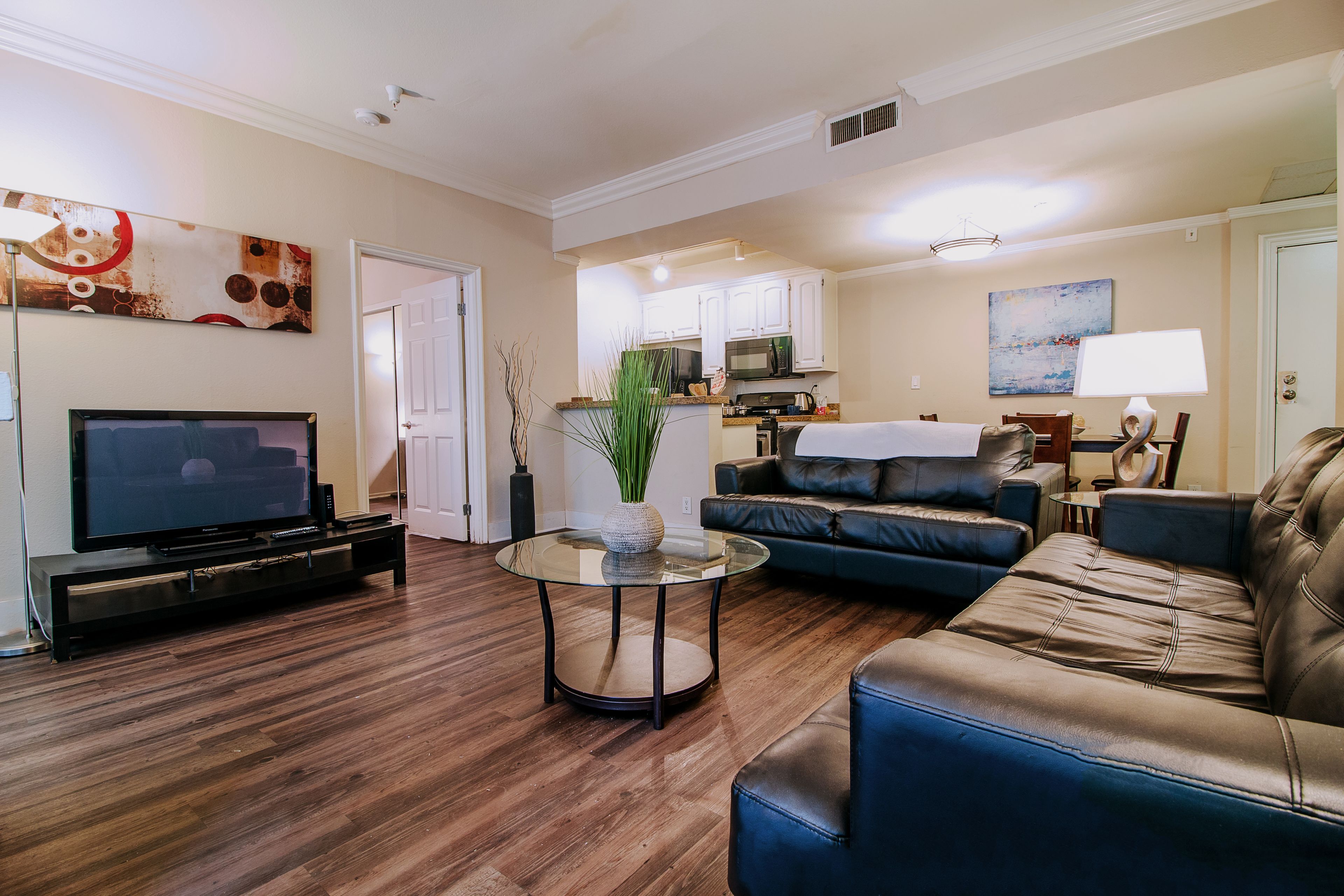 A living room with a TV, leather sofa, and a glass coffee table.
