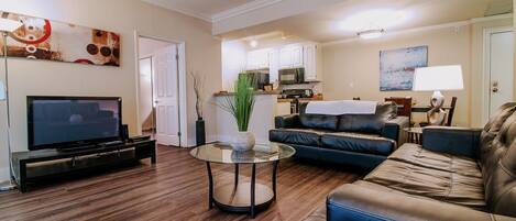 A living room with a TV, leather sofa, and a glass coffee table.
