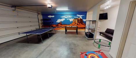 A room with a ping pong table, a foosball table, and a dartboard.