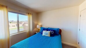 A bedroom with a large window, a bed with blue bedding, a nightstand with a lamp, and a view of the outside. - Cairn House - 4A7 (Moab)