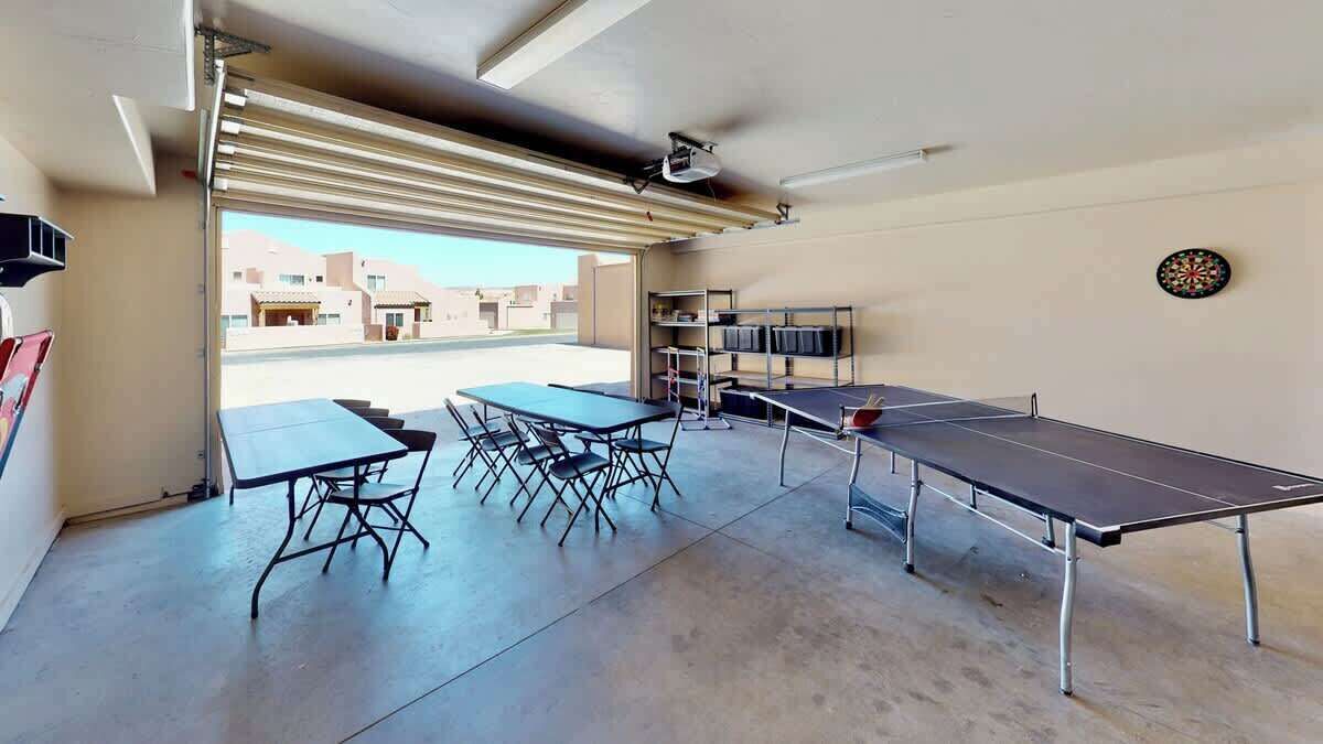 Una habitación con mesa de ping pong, una mesa de comedor con sillas y estanterías con libros.