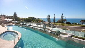 A swimming pool with a view of the sea, surrounded by greenery and a clear sky.