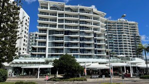 A modern multi-story hotel with balconies, a covered outdoor area, and a clear sky.