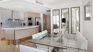 A modern kitchen with a central island, stainless steel appliances, and a dining area with a glass table and white chairs.