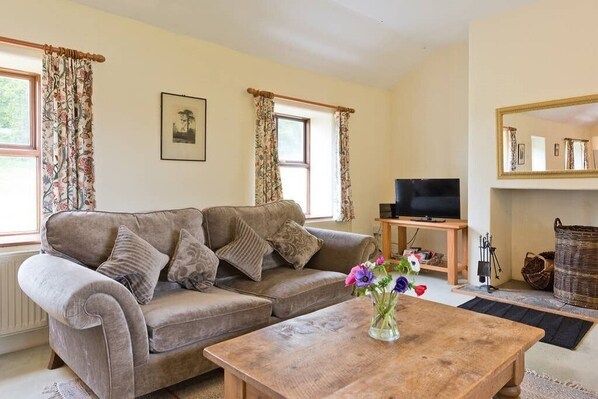 A living room with a sofa, a coffee table with a vase of flowers, a television on a stand, and a fireplace. - Spacious traditional Irish cottage, for golf and beach holidays. Pet friendly. (Baltray)