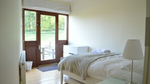 A bedroom with a bed, bedside table, lamp, and a view of a garden through a door. - Spacious traditional Irish cottage, on the banks of the Boyne. Pet friendly. (Baltray)