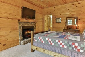 A log cabin bedroom with a stone fireplace, a bed with a quilt, a dresser, and a mirror.
