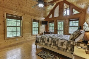Une chambre dans une cabane en bois, équipée d’un lit, d’une télévision et d’un ventilateur de plafond.
