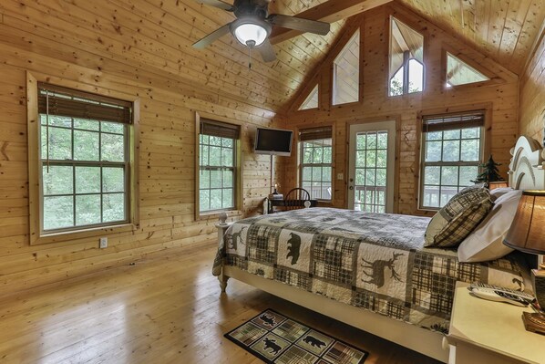 A wooden cabin bedroom with a bed, a television, and a ceiling fan.