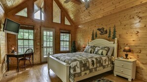 A cozy log cabin bedroom with a bed, a desk, and a television.
