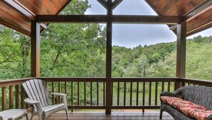 A covered deck with a wooden railing, a wicker sofa with a red cushion, and a white Adirondack chair.