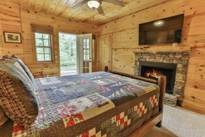 Ein Schlafzimmer in einer Blockhütte mit einem großen Bett, einem Kamin aus Stein und einem darüber montierten Fernseher.