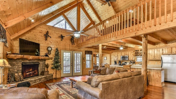 A spacious log cabin interior with a fireplace, a cozy seating area, and a kitchen.