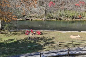 A lakeside area with a fire pit and red chairs.