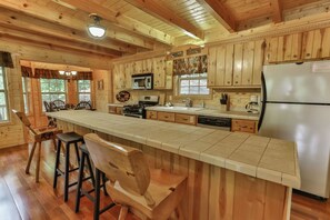 A wooden cabin kitchen with a long island counter, bar stools, a refrigerator, and a microwave.