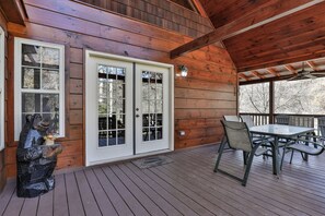 Une terrasse en bois avec une table et des chaises, une sculpture d’ours et une porte blanche avec des panneaux de verre.