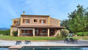Une maison à deux étages avec une façade en pierre, une piscine et un espace salon extérieur.