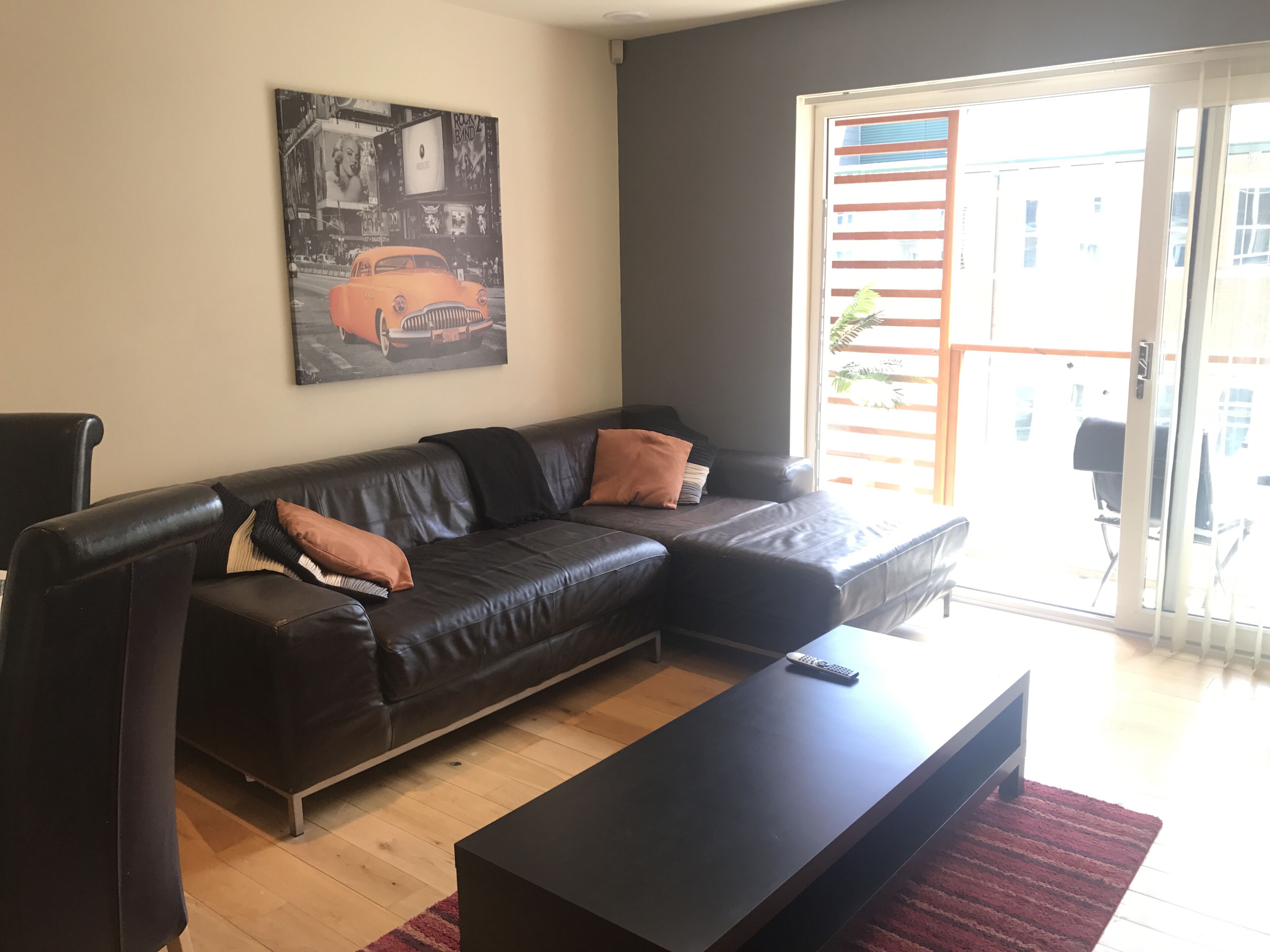 Een woonkamer met een zwarte leren bank, een rood vloerkleed en een schilderij aan de muur.