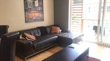 Een woonkamer met een zwarte leren bank, een rood vloerkleed en een schilderij aan de muur.