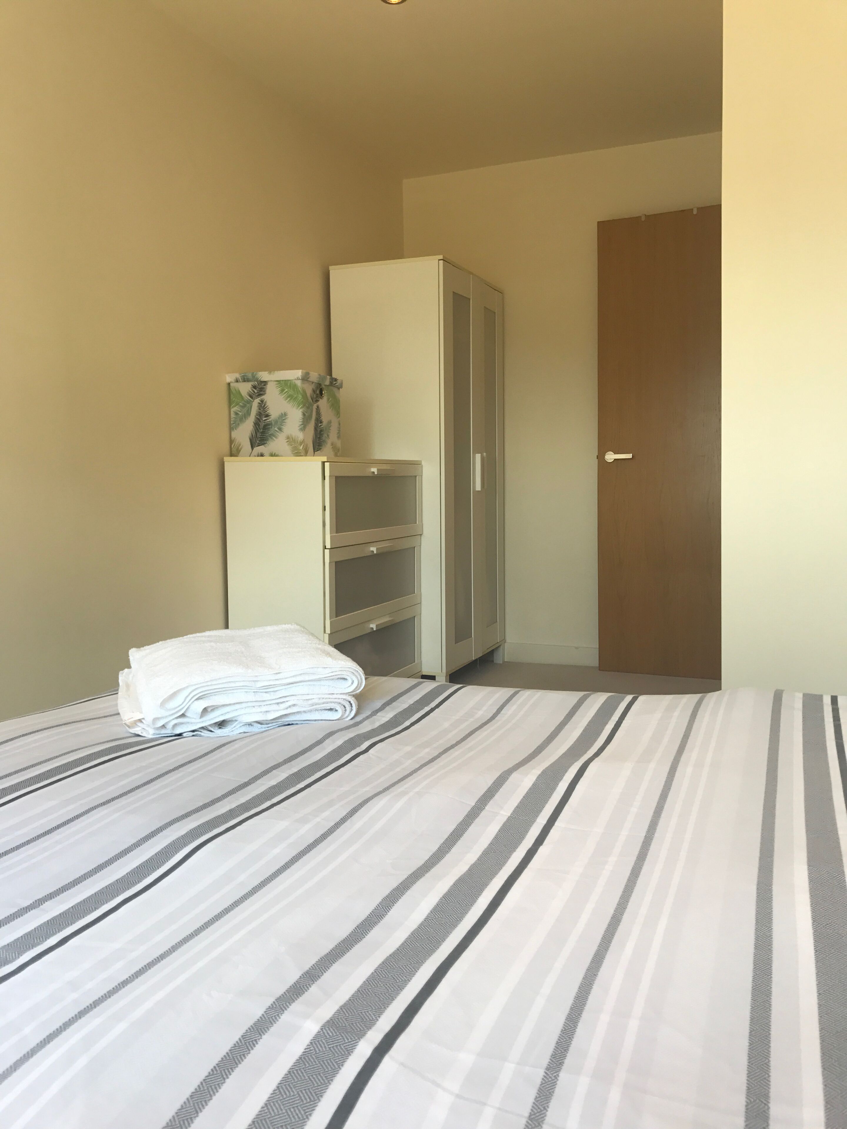 Ein ordentlich bezogenes Bett mit Streifenmuster, ein Schrank mit Spiegel und eine Tür.