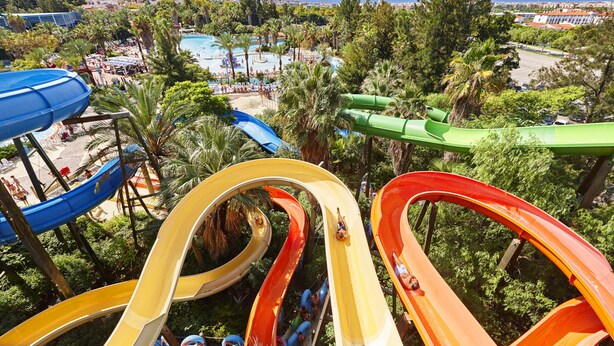 A water park with multiple water slides and a view of the surrounding area including a beach and buildings. - Alexis II Zeus Salou 0632 (Salou)