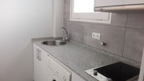A compact kitchen with a stainless steel sink, a built-in washing machine, and a built-in stovetop. - Alexis II Zeus Salou 0632 (Salou)