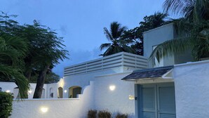 Eine moderne Villa mit weißer Fassade, einer blauen Tür und einem kleinen Gartenbereich mit Pflanzen und einem Betonweg.