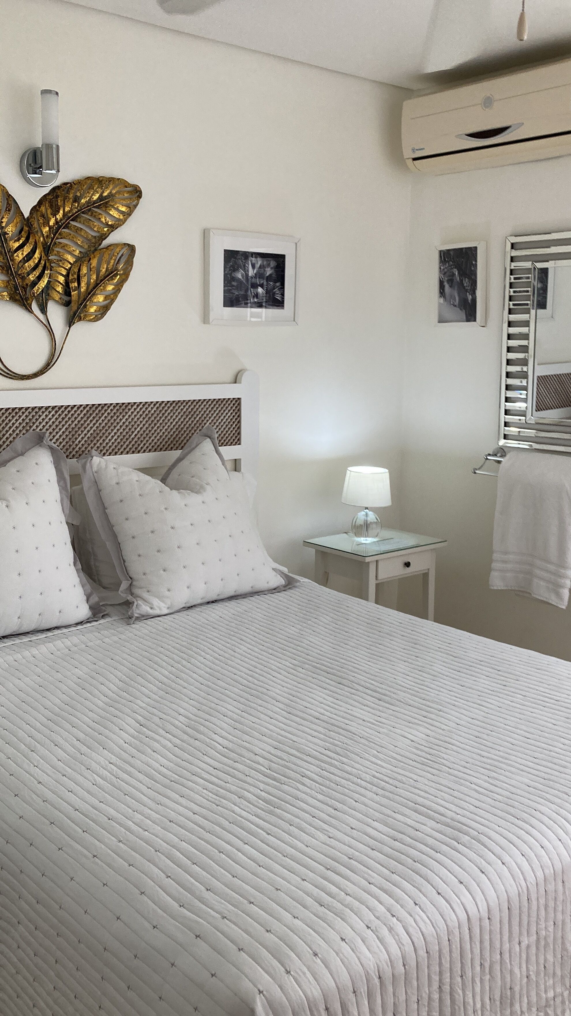 A neatly arranged bedroom with a large bed, a bedside table with a lamp, and a wall-mounted air conditioner.