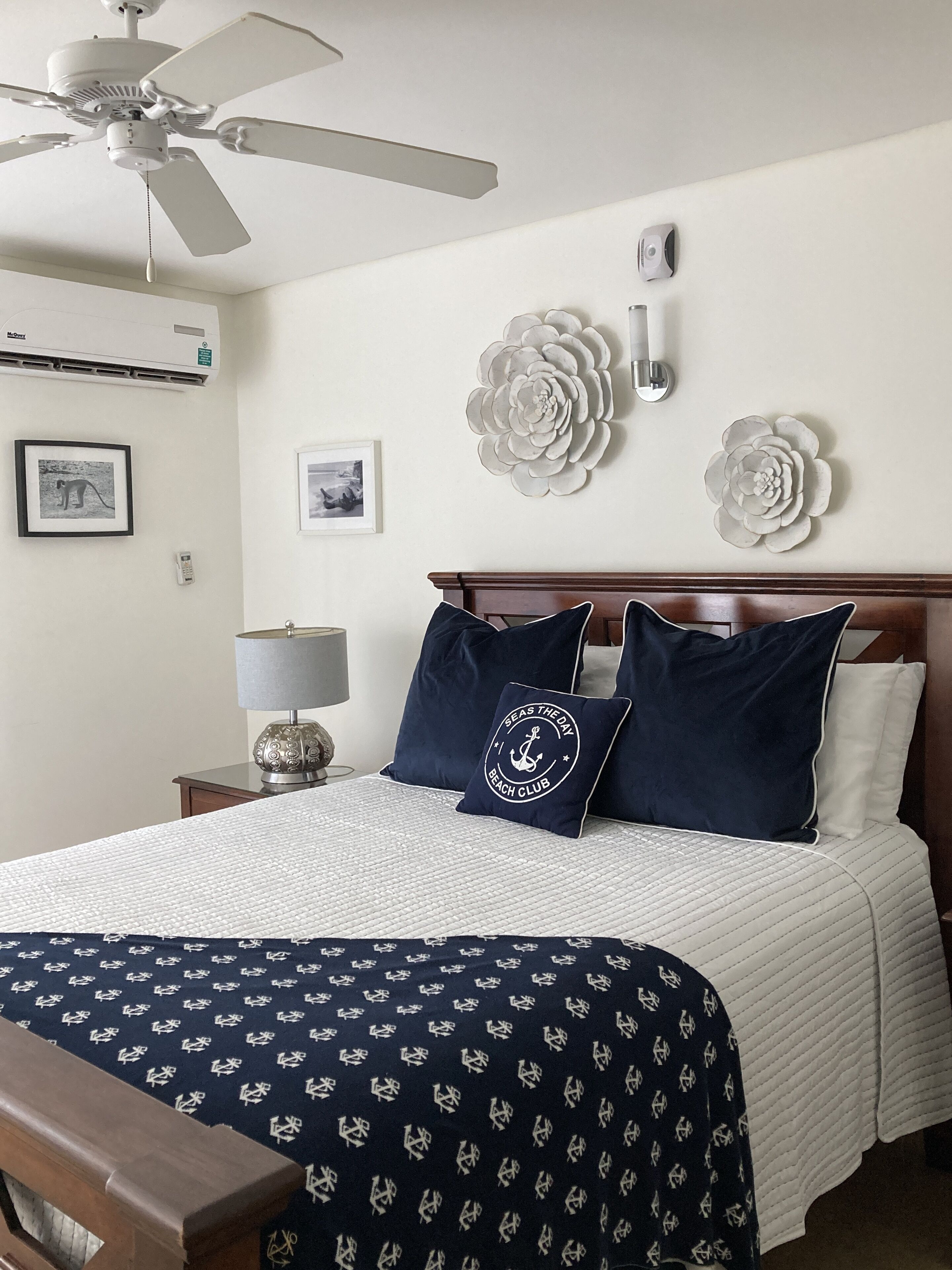 A neatly arranged bedroom with a bed, a nightstand, a lamp, a ceiling fan, and wall decorations.
