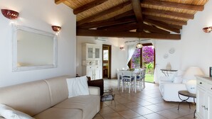 A living room with a sofa, dining table, and chairs, a kitchen area, and a view of a garden.