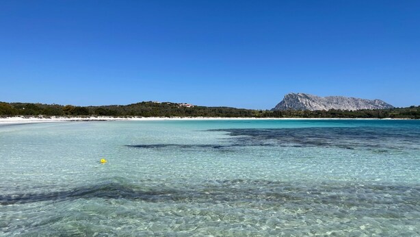 A clear coastal view with a mountain in the background.