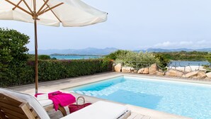 A poolside area with a wooden deck, a white umbrella, and a lounge chair.