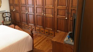 Un dormitorio con un armario de madera grande, una cama con colcha estampada, una silla y una mesita con un juguete.