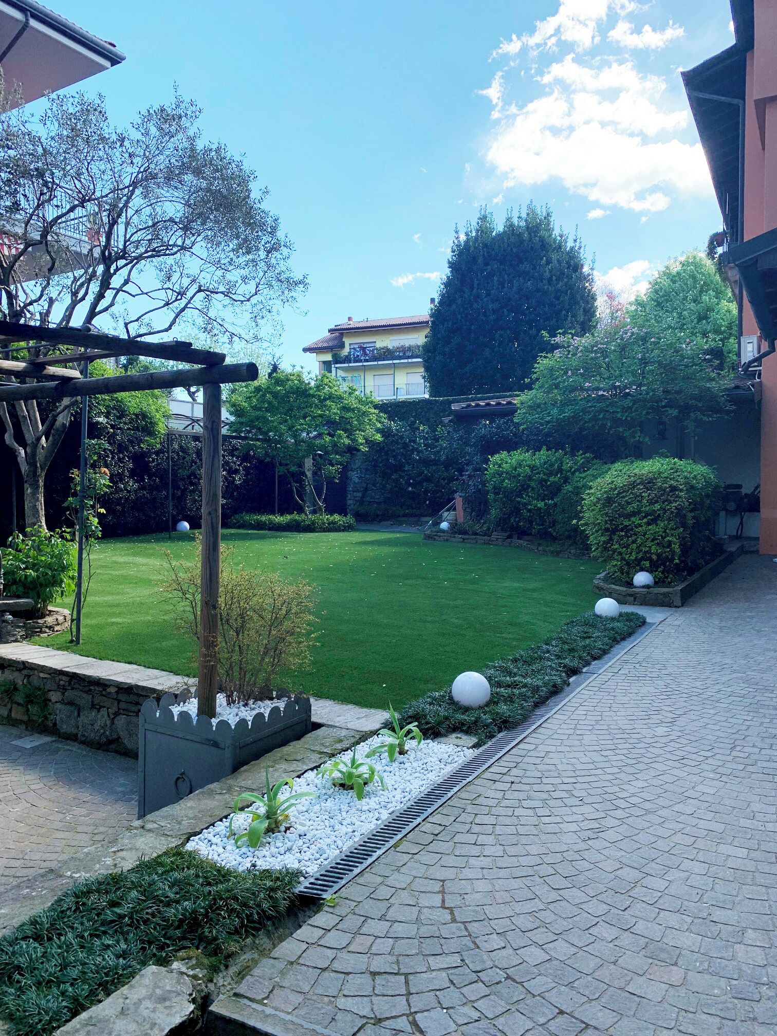 Un cortile con un vialetto lastricato, un prato e una struttura pergolata.