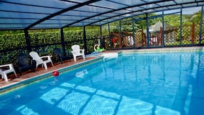 Une piscine intérieure à l’eau d’un bleu cristallin, entourée de chaises en plastique blanc et protégée par une paroi en verre.