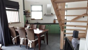 Un coin repas avec une table et des chaises en bois, une cuisine à l’arrière-plan et un escalier.
