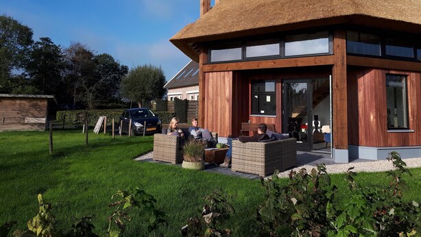 Une maison moderne avec un toit de chaume, un revêtement extérieur en bois et de grandes fenêtres.