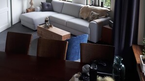 Un salon moderne avec un canapé d’angle, une table à manger et un plafond haut avec des poutres apparentes.