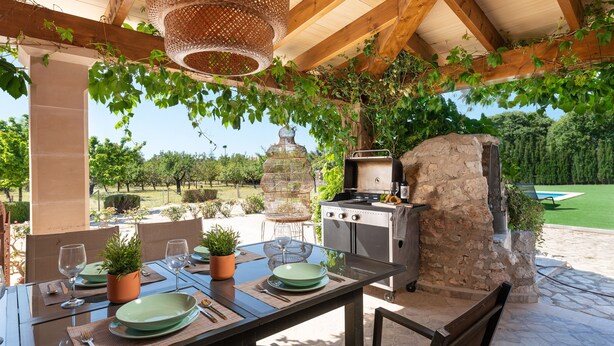 An outdoor dining area with a table set for four, a grill, and a stone wall. - SES VELES - Villa with private pool in Lloseta. (Lloseta)