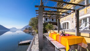 Une terrasse offrant une vue dégagée sur un lac, une pergola en bois et une table dressée avec une nappe jaune.
