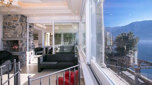 Un salon moderne avec une cheminée en pierre, une porte vitrée donnant sur un balcon et une vue sur un lac et des montagnes.