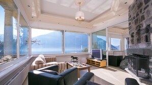 Un salon spacieux doté d’une cheminée, de grandes fenêtres et offrant une vue sur les montagnes.