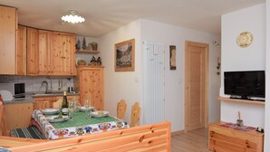 A compact kitchen with wooden cabinets, a dining table set for four, a built-in TV, and a radiator.