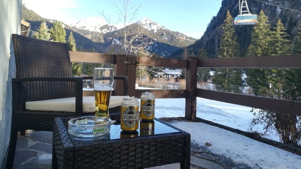 A balcony with wicker furniture, a glass table, and two cans of beer.