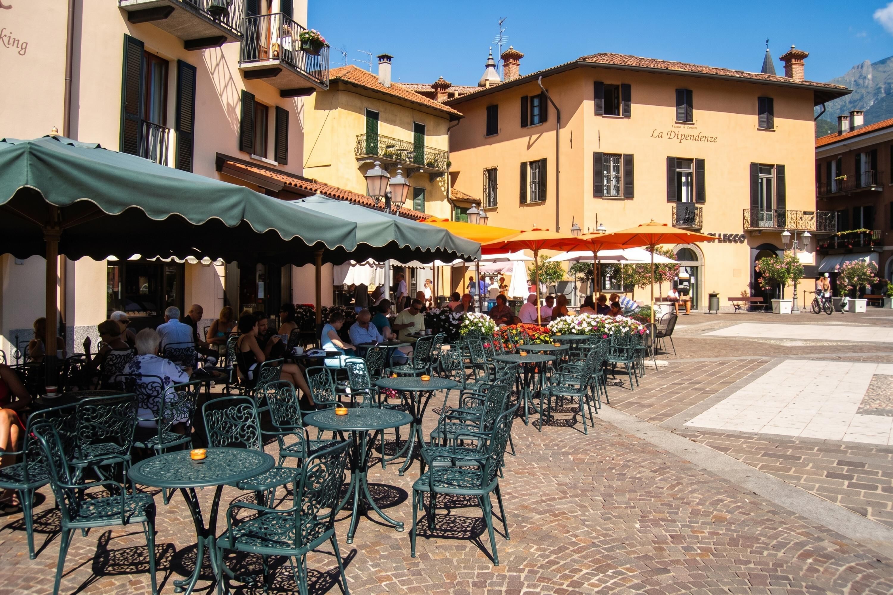 Outdoor seating with tables and chairs, a cobblestone street, and buildings with balconies.
