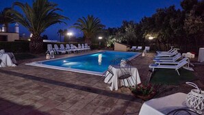 A swimming pool with lounge chairs and tables, surrounded by palm trees and a night sky. - Exclusive Villa with Private Pool and Etna View (Piedimonte Etneo)