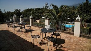 An outdoor patio with metal tables and chairs, a decorative vase, and a view of a swimming pool and mountains in the background. - Exclusive Villa with Private Pool and Etna View (Piedimonte Etneo)